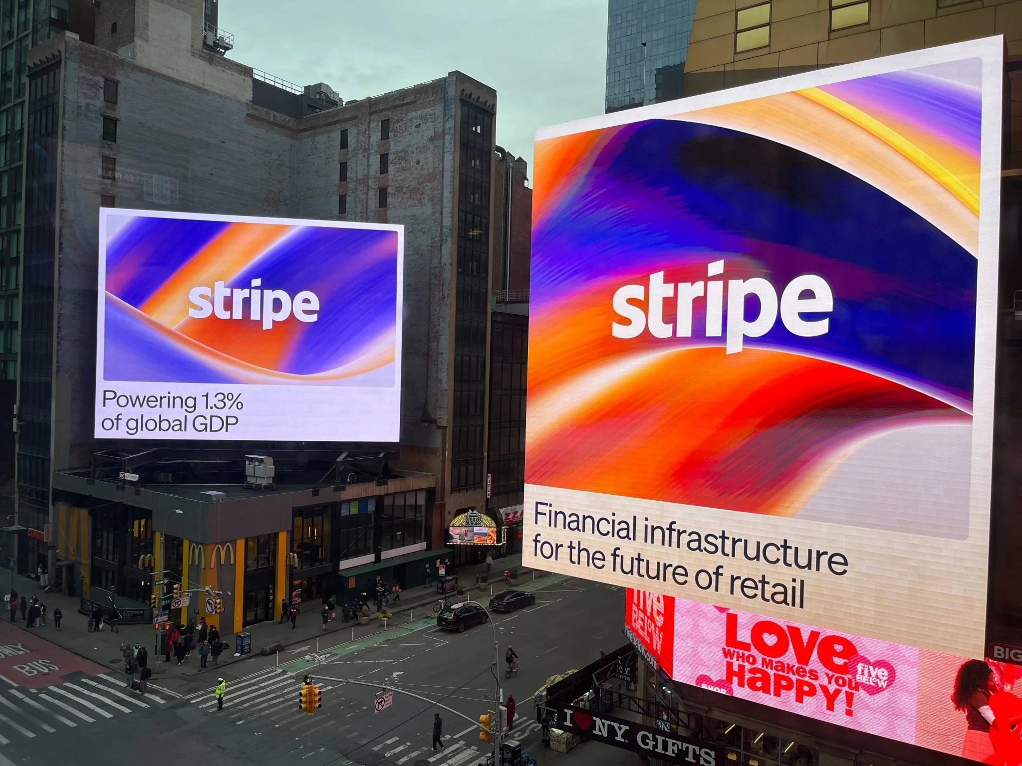 Two large Stripe billboard advertisements displayed on buildings in Times Square, New York City. The left billboard reads &lsquo;Powering 1.3% of global GDP&rsquo; and the right reads &lsquo;Financial infrastructure for the future of retail,&rsquo; both featuring a colorful abstract gradient in blue, orange, and red.