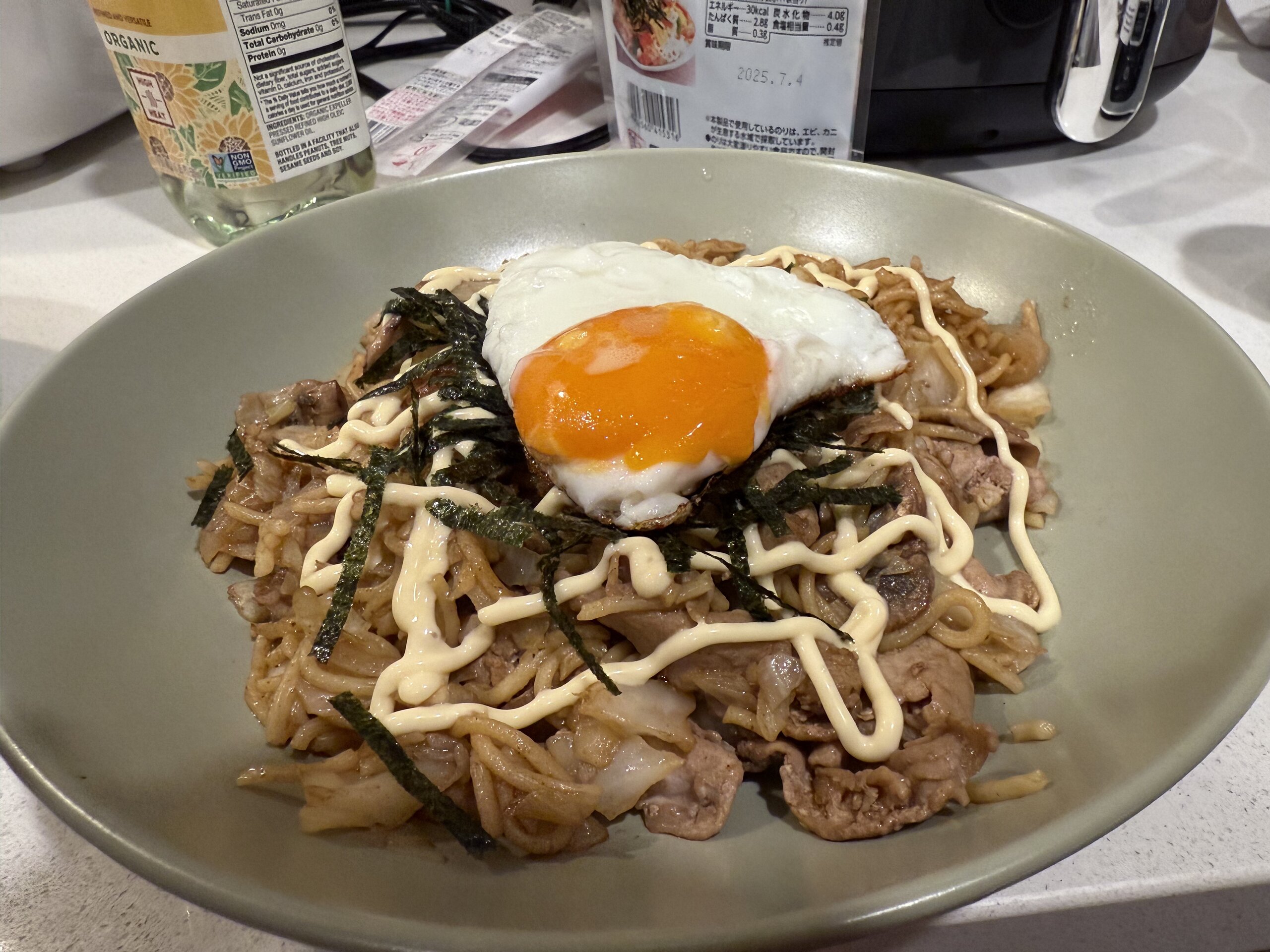 日式炒麵上覆蓋海苔、日式美乃滋和太陽蛋，擺放在淺綠色餐盤中。