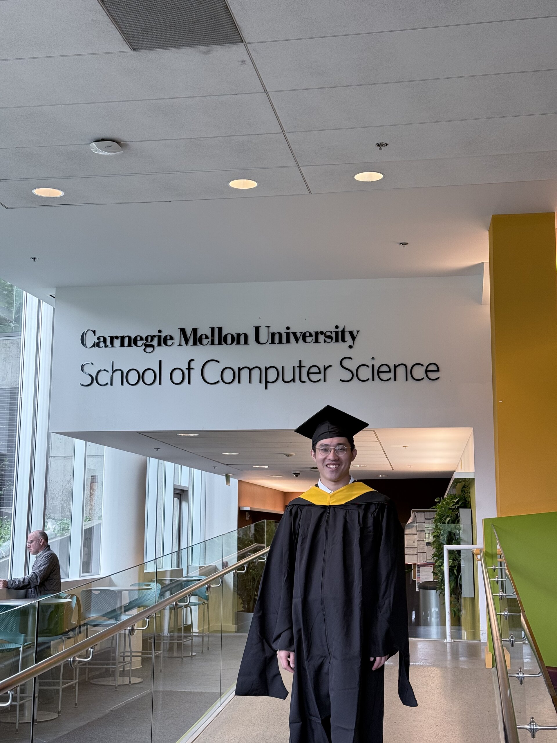 Tomy 穿著學士袍,站在 CMU School of Computer Science 的標誌下微笑合照。