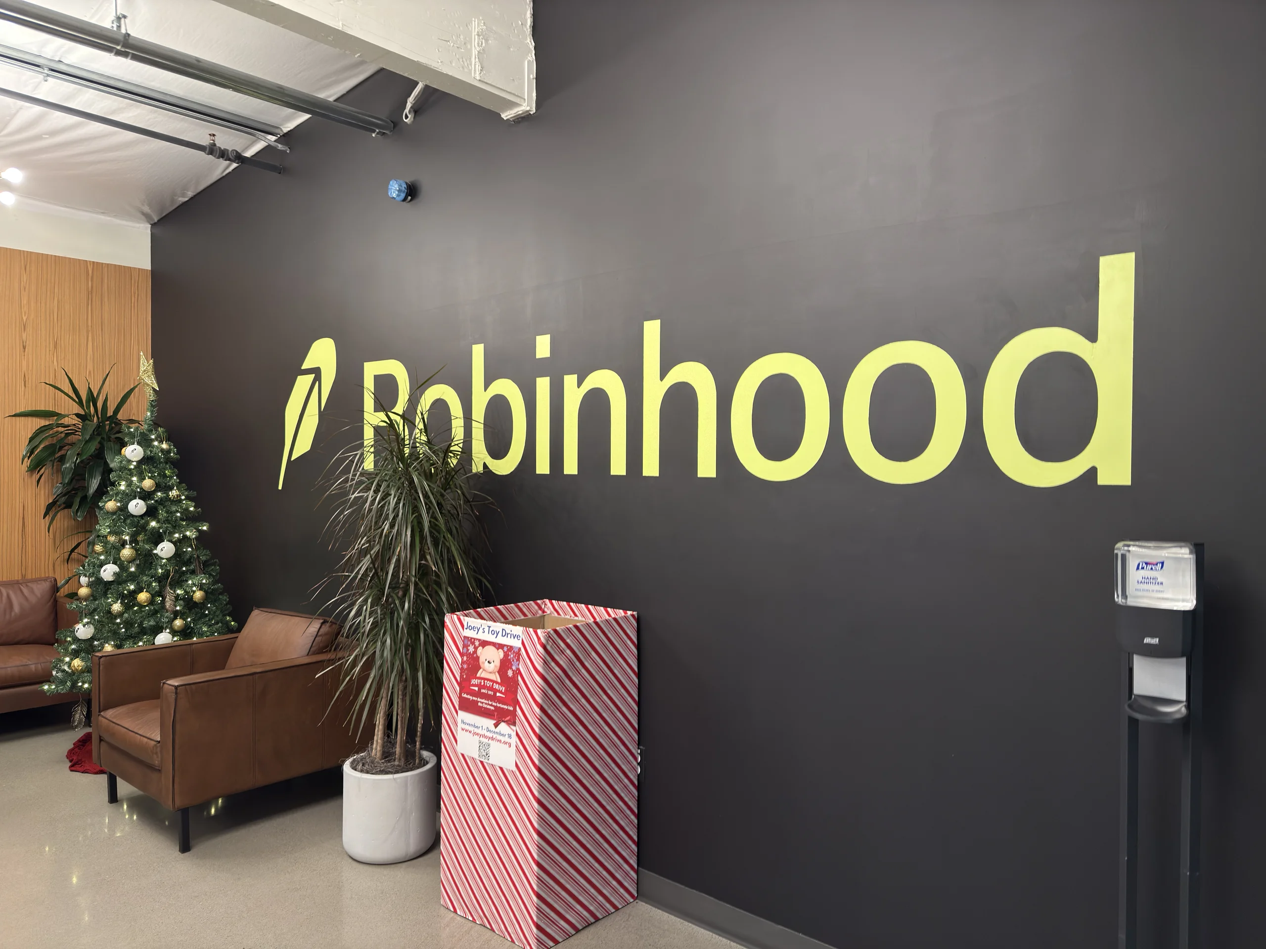 Robinhood 辦公室內牆面,綠色 Robinhood 標誌旁放置聖誕樹與捐贈箱