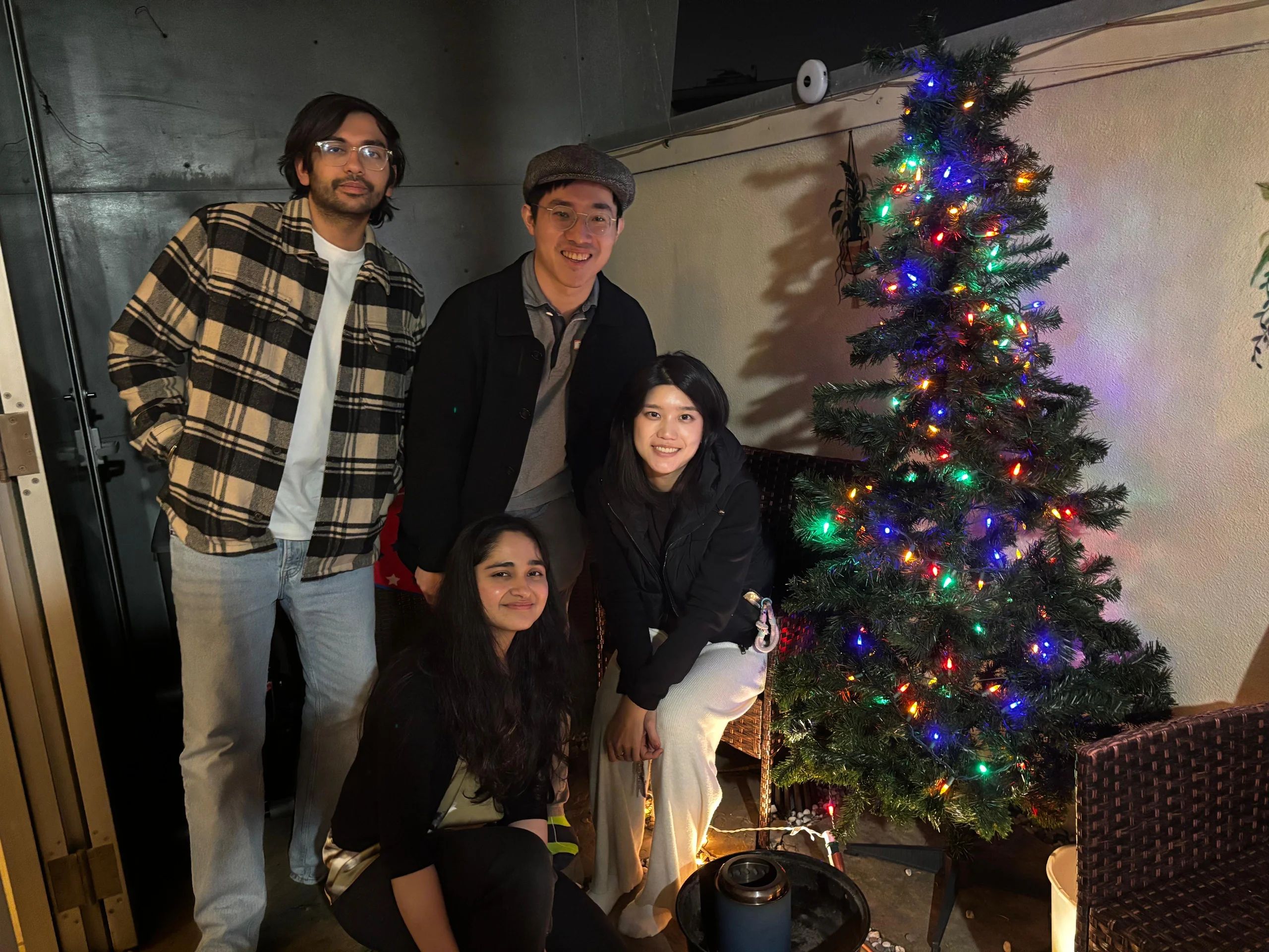 多人在室內聖誕樹旁合影,樹上掛滿彩色燈飾,氣氛溫馨