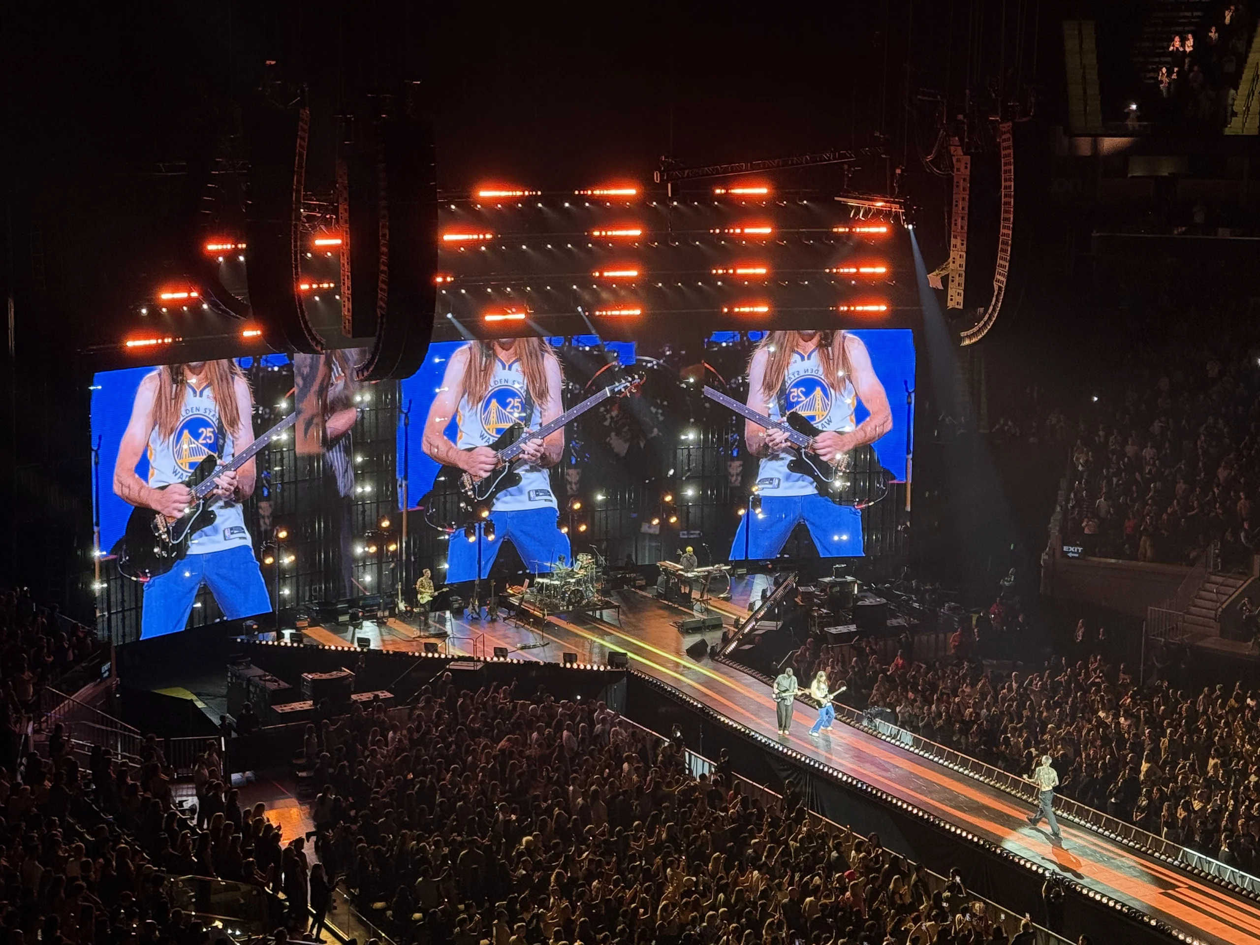 演唱會現場，吉他手在螢幕上穿著勇士隊球衣表演