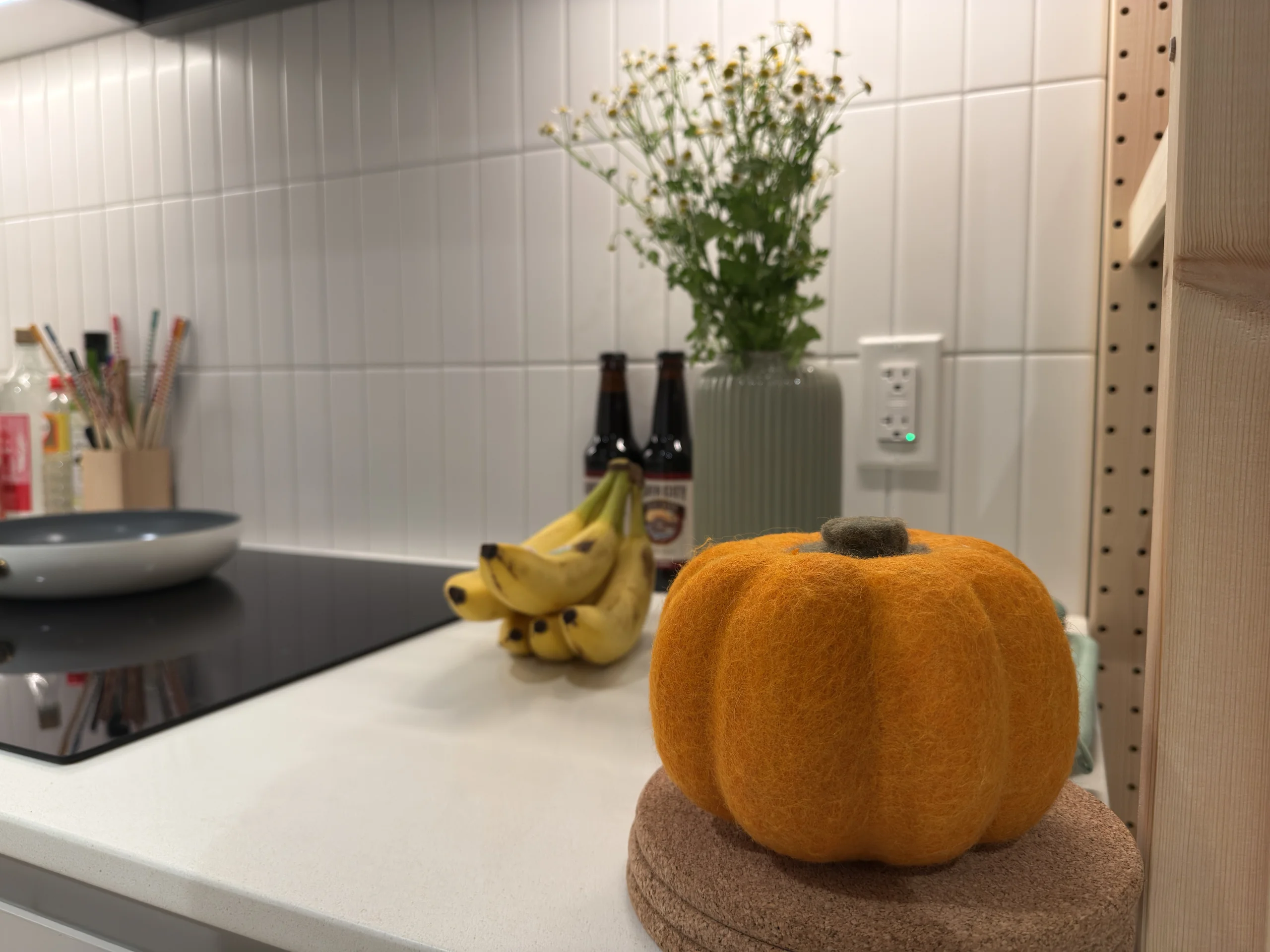 廚房角落擺著橘色毛氈南瓜與香蕉,背景是白色磁磚牆