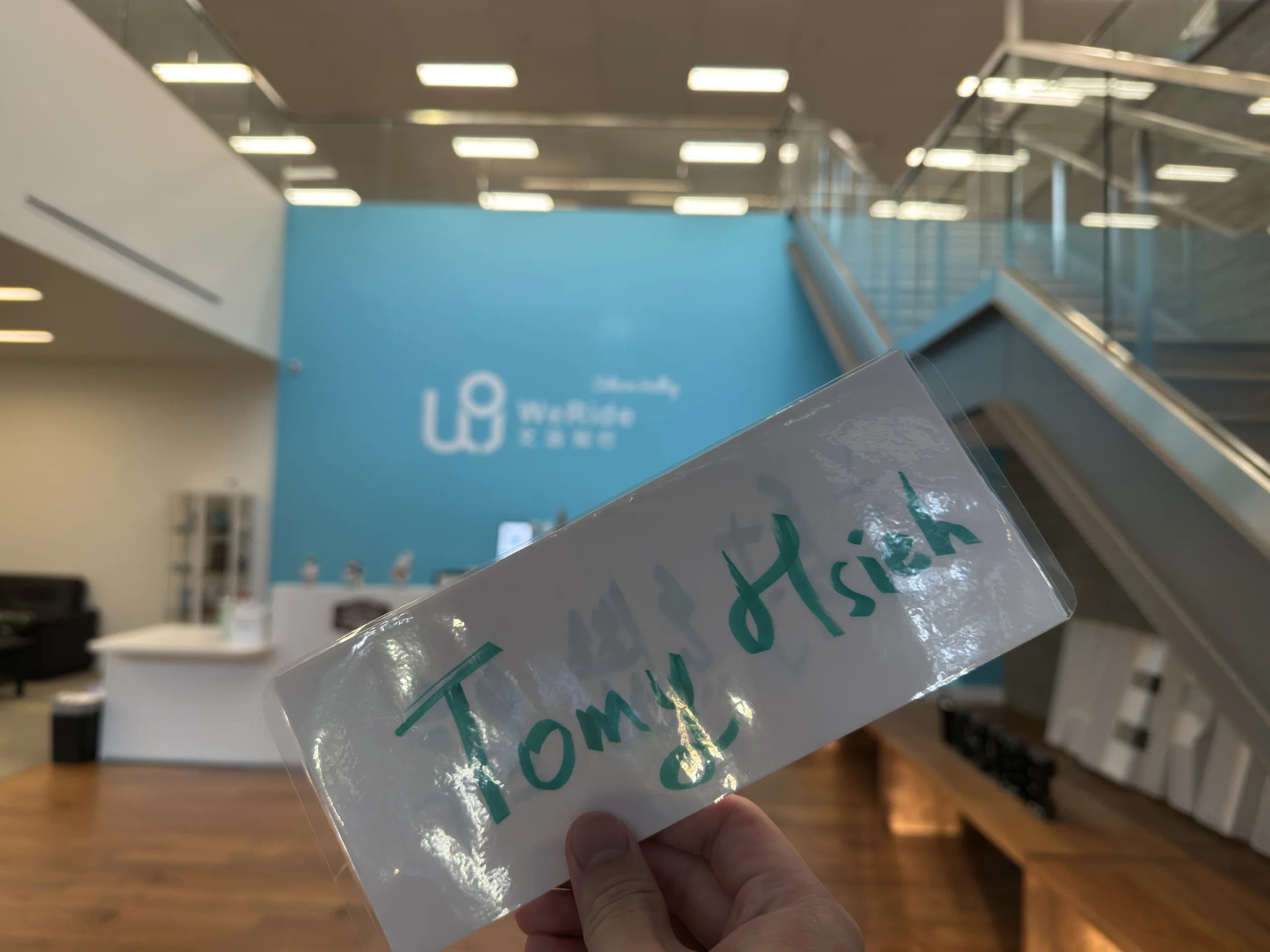 手持名牌寫著 Tomy Hsieh，背景是 WeRide 接待大廳