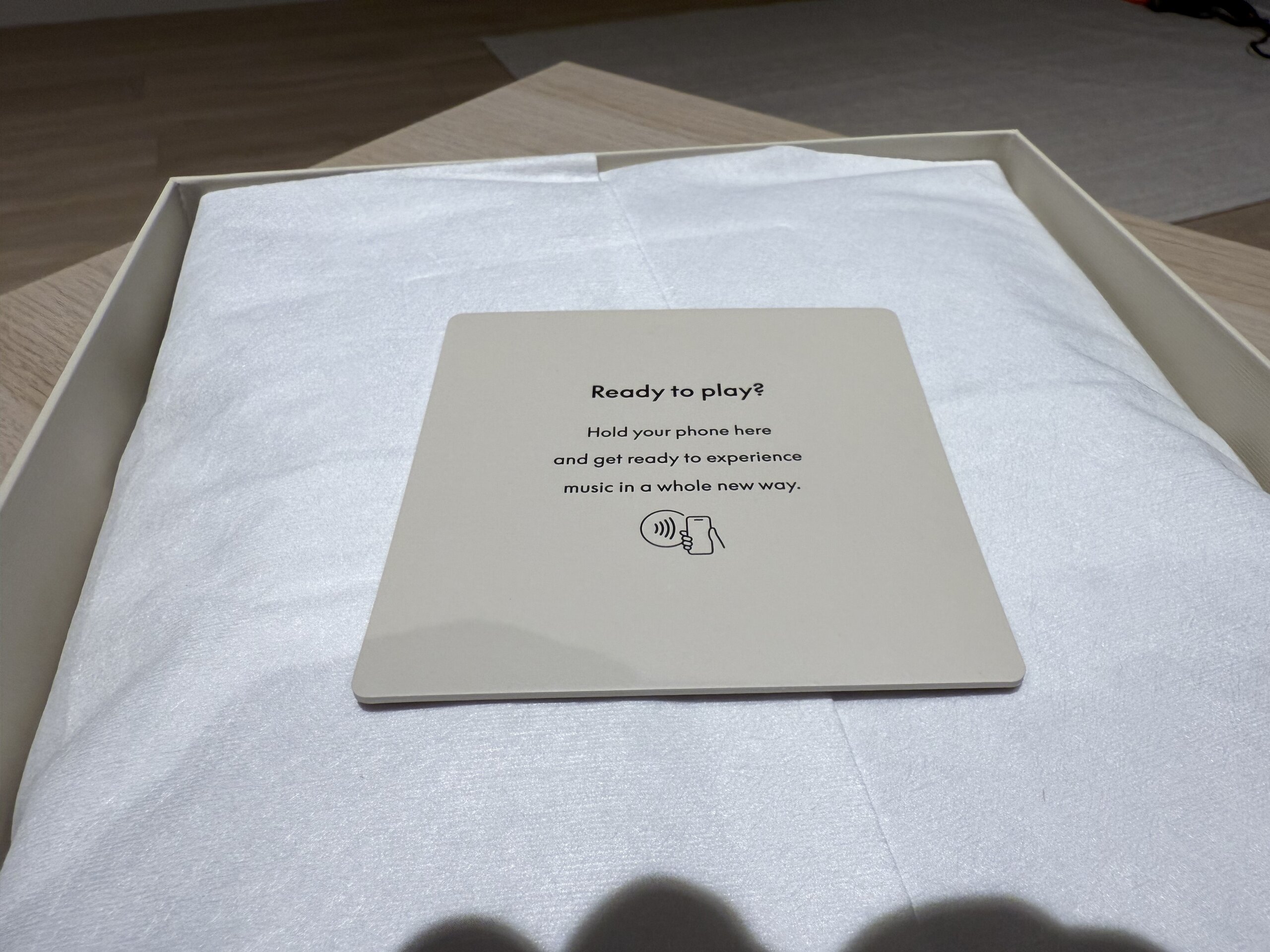 Beoplay H100 包裝內卡片的背面，印有『Ready to play? Hold your phone here and get ready to experience music in a whole new way』，以及感應標誌。