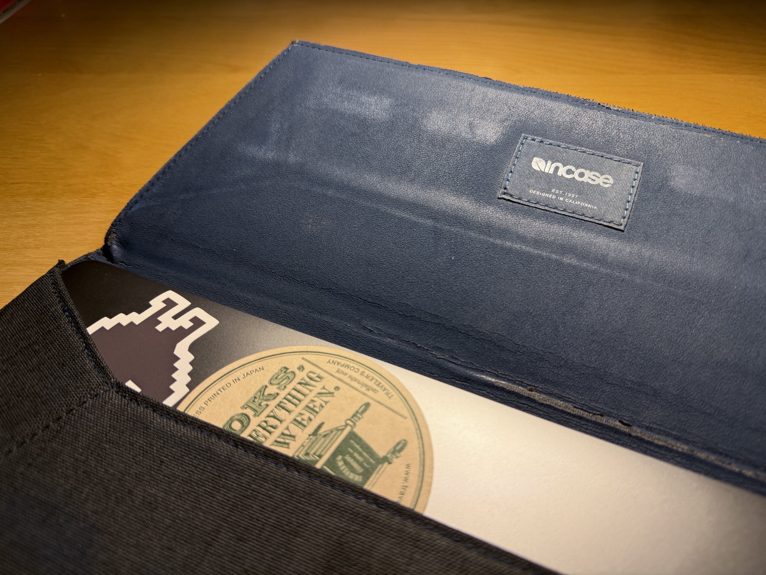 黑色 Incase 電腦保護套打開的樣子，裡面放著有貼紙裝飾的 MacBook Pro